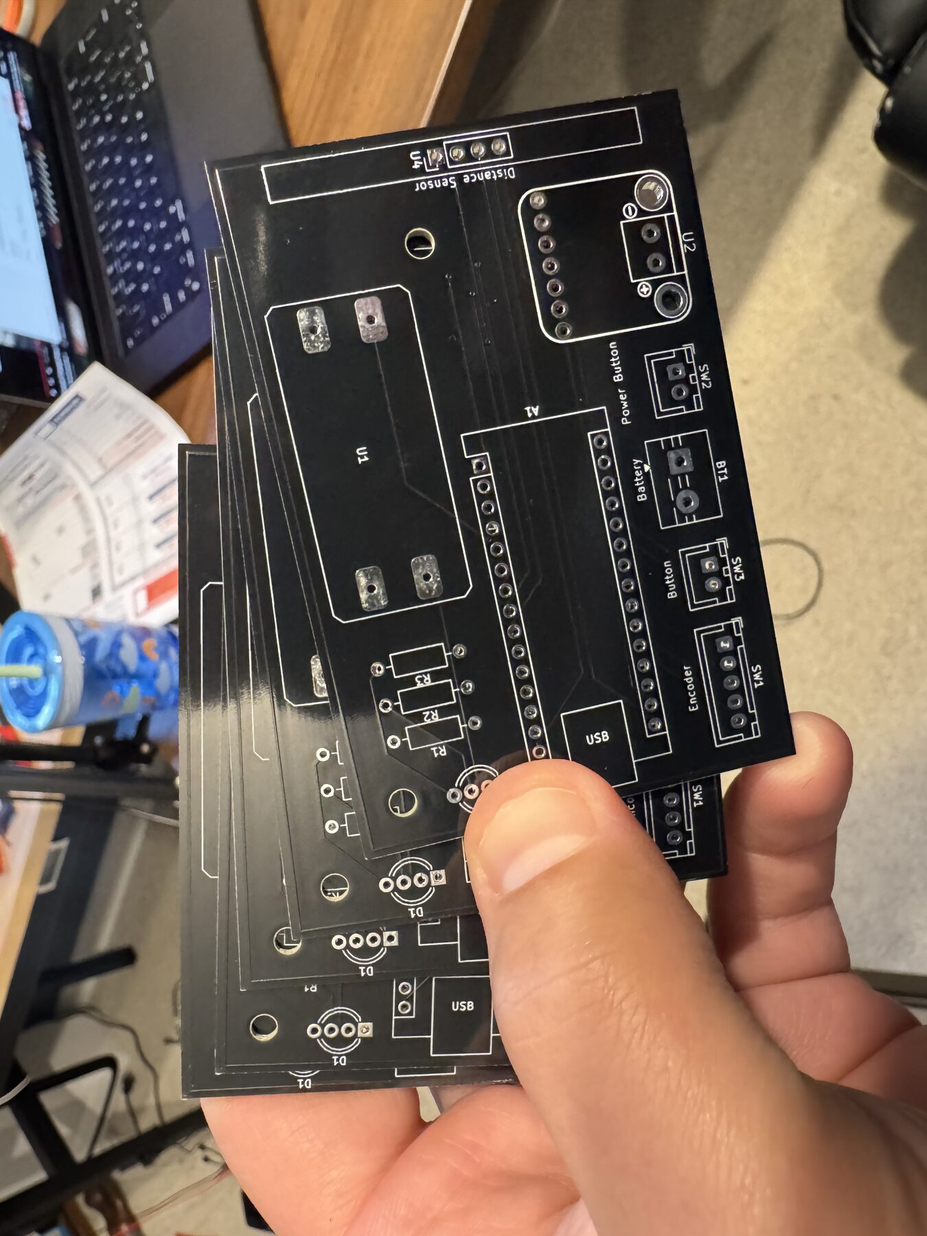 A stack of bare black PCBs held in one hand