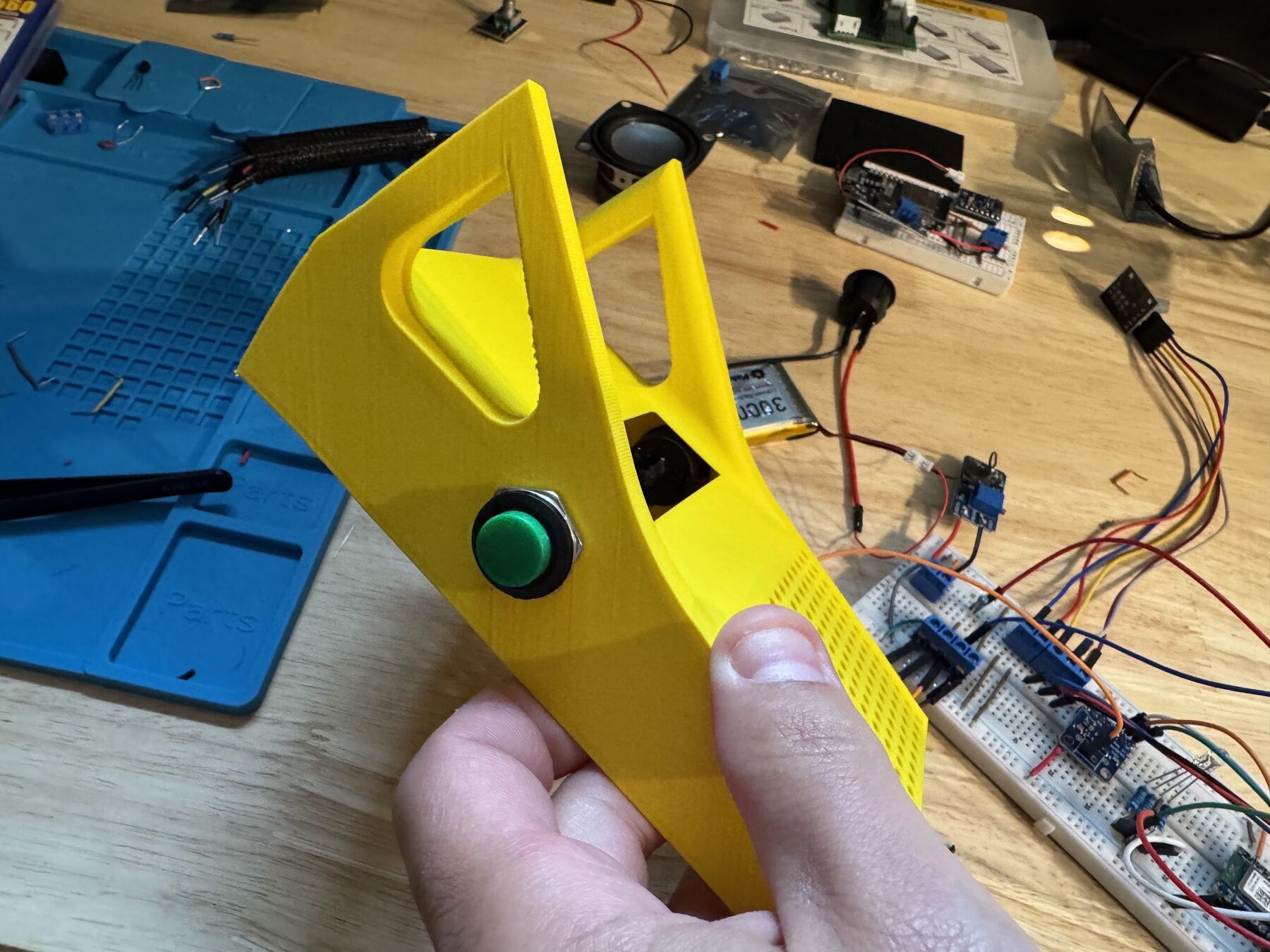 The yellow case from the side, with a green push button, next to the breadboard prototype