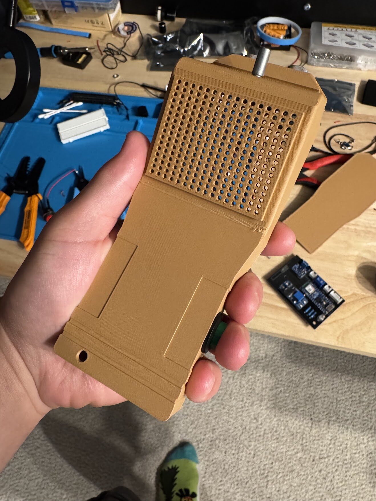 The printed tan case held in one hand, showing the speaker grille and knob