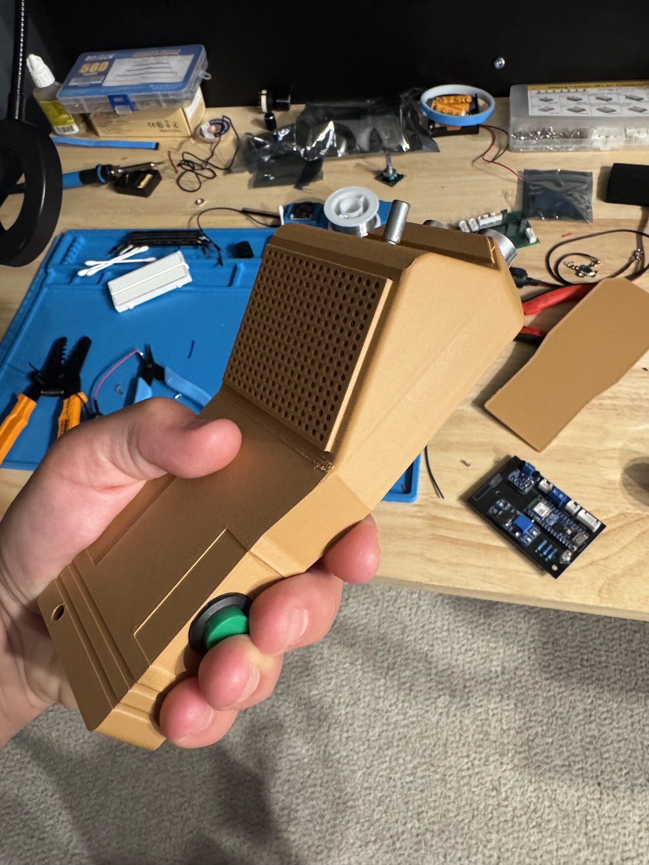 The tan case held at an angle, with the soldered PCB on the desk behind it