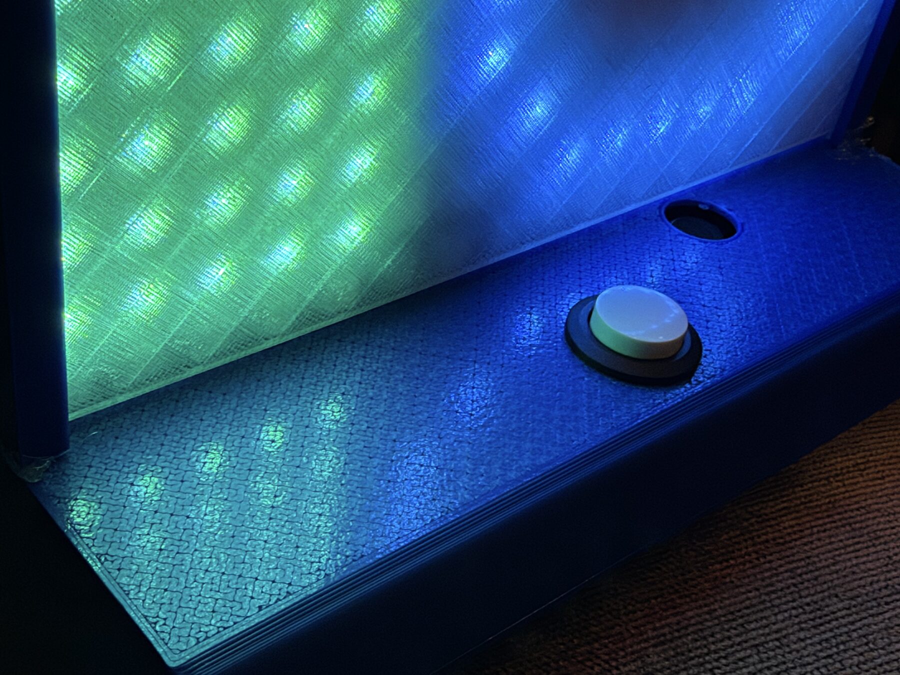 Close-up of the push button and mic hole on the blue base, lit green and blue from the panel