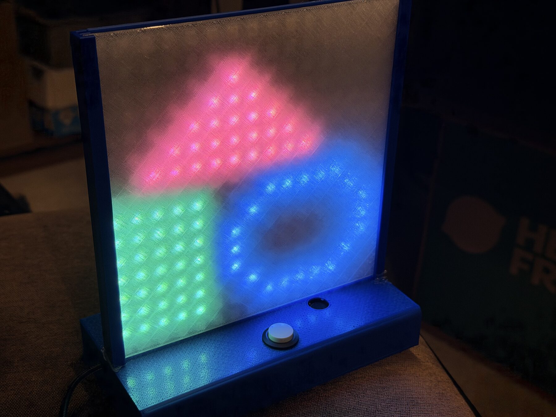 The toy lit up with a pink triangle, green square and blue ring behind the frosted diffuser